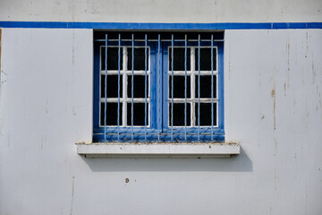 Old vintage 19th century wood blue window, with large blue  metal window protection bars, on white rustic house wall
