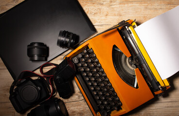 Vintage journalistic equipment material consisting of a typewriter, laptop, camera and photo lenses on a rustic desk 