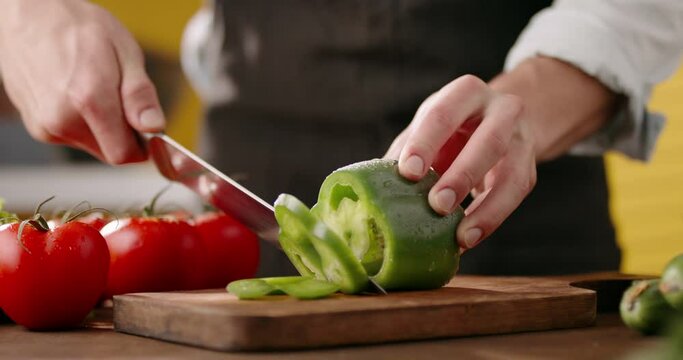 Close up shot of chef's hands using a knife cutting a fresh bell pepper on wooden board. Cooker preparing a vegetarian meal - food and drink 4k footage