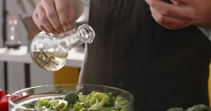 Chef adding olive oil into a bowl of fresh healthy green salad. Cooker preparing a vegetarian mediterranean meal, using natural ingredients food and drink close up 4k footage