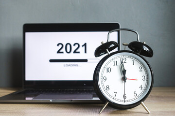 Close up of alarm clock countdown with loading the new year 2021 on a laptop screen on a wooden table with grey background. 