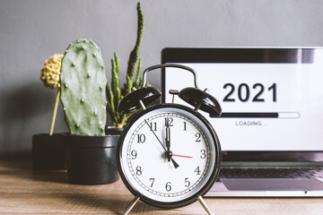 Close up of alarm clock countdown with loading the new year 2021 on a laptop screen and decorative plant on a wooden table with grey background. 