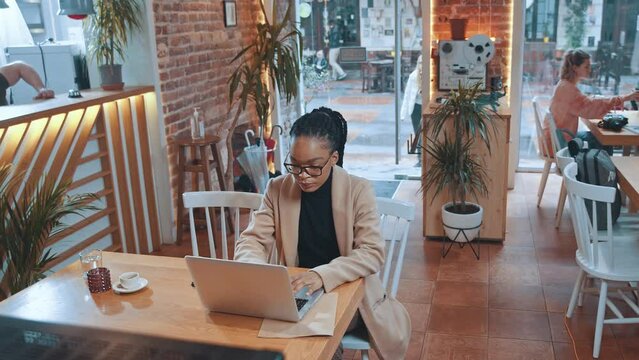 Afro-american attractive woman freelancer working on laptop computer in coffee house. Modern cafe interior. Young businesswoman. Cozy workspace.