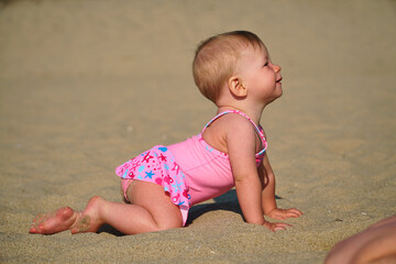 The kid learns to crawl. The child is crawling along the sand. First steps and first vacation. High quality photo