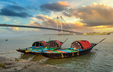 Boats at Ganges river bank with view of a suspension bridge known as Vidyasagar Setu at Kolkata India at sunset