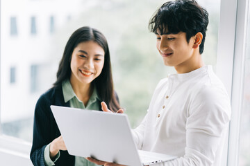 Obraz premium Two Asian colleagues are discussing the work. The businessman is holding a laptop in his hand