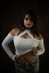 Studio portrait of a beautiful and young Indian Bengali female model in white cold shoulder top and jeans hot pant. Indian fashion and models