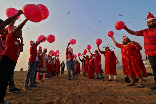 People wearing Santa hats wave balloons as they take part in a laughter yoga session during Christmas celebrations on a beach in Mumbai