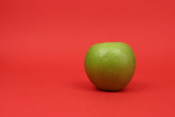 Healthy eating concept. Green apple wrapped by measuring tape on red background