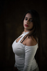 Obraz na płótnie Canvas Studio portrait of a beautiful and young Indian Bengali female model in white cold shoulder top and jeans hot pant. Indian fashion and models