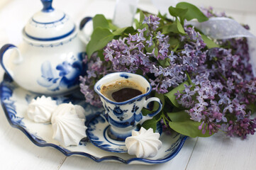 Obraz na płótnie Canvas lilac flowers, sugar bowl, cup of coffee, meringues on a tray on a light background