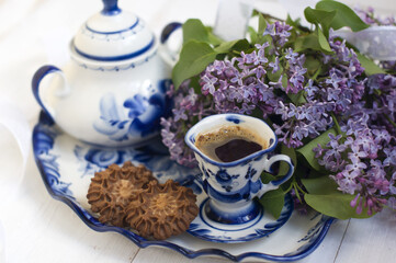 lilac flowers, sugar bowl, cup of coffee, meringues on a tray on a light background. concept with lilac