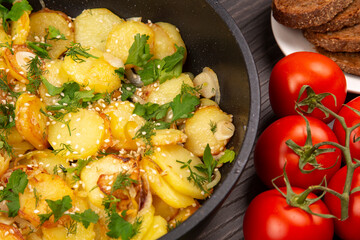 cooked fried potatoes with herbs, spices and vegetables in a black pan on a wooden table