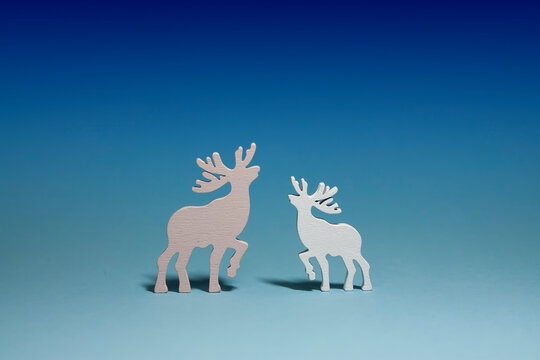 Horizontal conceptual studio subject photo with two wooden isolated deer toys of white and pink colours, looking to each other, on light blue gradient background