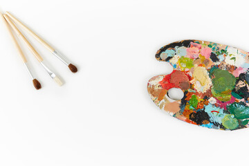 Artist's palette and brushes with different colors isolated on a white background
