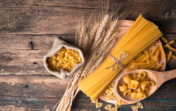 Pasta and wheat ears on a cutting Board on a wooden background. Top view with space to copy. Concept of products, culinary backgrounds.