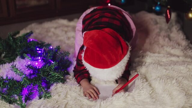 a child in red clothes is sitting waiting for the new year. the concept of celebrating Christmas at midnight. holiday costume. a girl writes a letter to Santa Claus. wish list