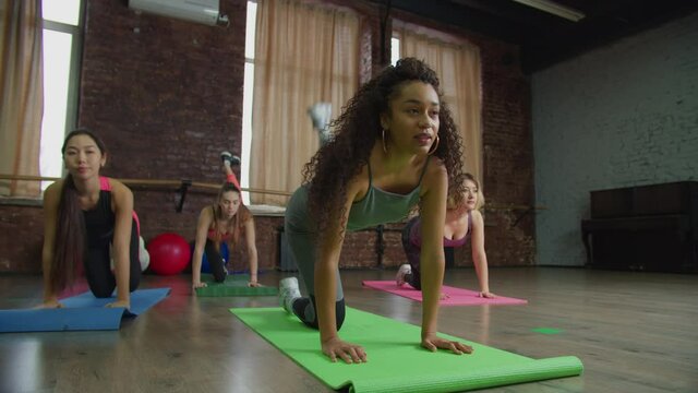 Active motivated attractive multiethnic diverse sporty fit women training and strengthening hip and buttocks muscles, performing fire hydrant and donkey kick exercises during intense workout at gym.