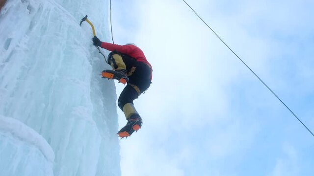 Alpinist man with ice tools axe climbing a large wall of ice.
