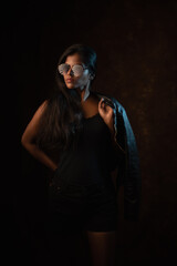 Fototapeta na wymiar Studio portrait of a beautiful and young dark skinned Indian Bengali female model in black camisole and black leather jacket. Indian fashion and models