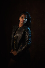 Studio portrait of a beautiful and young dark skinned Indian Bengali female model in black camisole and black leather jacket. Indian fashion and models