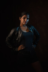 Studio portrait of a beautiful and young dark skinned Indian Bengali female model in black camisole and black leather jacket. Indian fashion and models