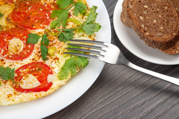 cooked fried omelet with herbs and vegetables in a white plate on a wooden table