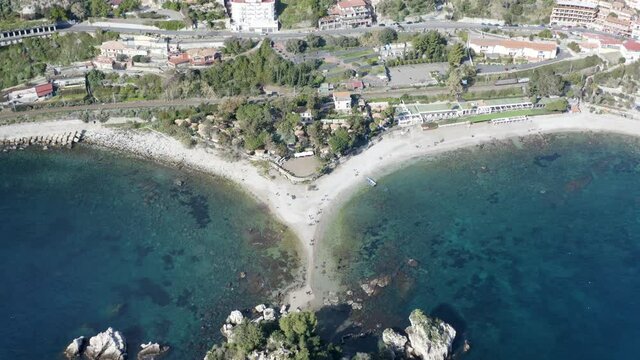 Aerial view of Isola Bella in Taormina in Sicily, Italy. The small island is connected to the mainland by a narrow strip of white sand and surrounded by the turquoise colored water of the Ionian Sea.