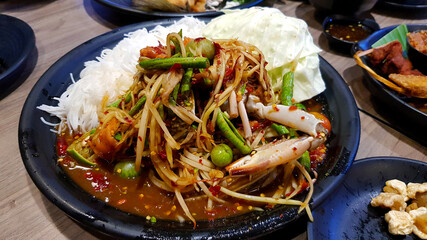 Close up Thai spicy seafood papaya salad with salted crab and fermented fish mixed with white rice noodle on black dish or plate. Famous food in Thailand and Delicious meal.