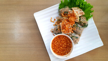 Top view of Vietnamese steamed rice-skin dumplings, green cabbage leaf and fried onion on top with sweet peanut bean sauce in white dish or plate. Asian food on wooden table, Famous meal in Vietnam.