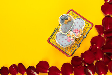 flat lay, several fabric hearts lie in a shopping basket on an orange background near rose petals. Concept to celebrate valentine's day. Copy space.