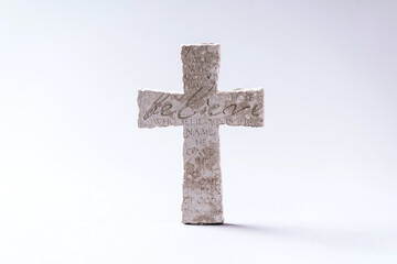 Stone cross with inscription Believe on grey background, Copy space. Christian backdrop. Biblical faith, gospel, salvation concept