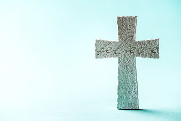 Stone cross with inscription Believe on blue background, Copy space. Christian backdrop. Biblical...