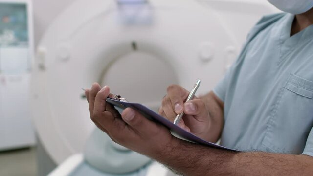 Mid-section PAN of unrecognizable male tech filling medical form in CT scan room