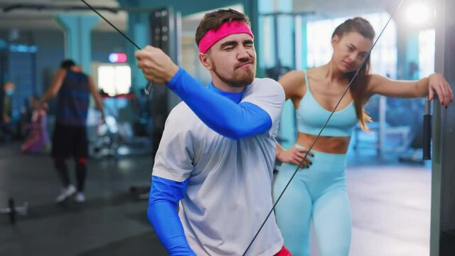 Funny caucasian tricky man lifting weights in the training room being very lazy flirting to girls. Gym concept. Comical workout scene.