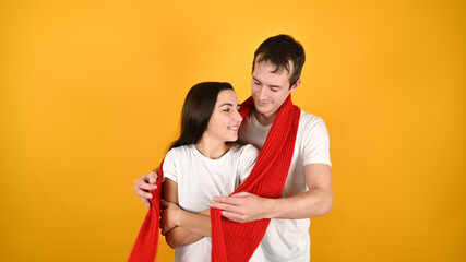 Lovely young couple hugging. Portrait of happy young couple with red warm scarf on yellow background. Valentine's Day celebration