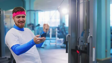 Weak lazy funny sportsman beginner using amrtphone while exercising with gym eqipment. Fun and humor concept. Fitness parody.fake athlete.