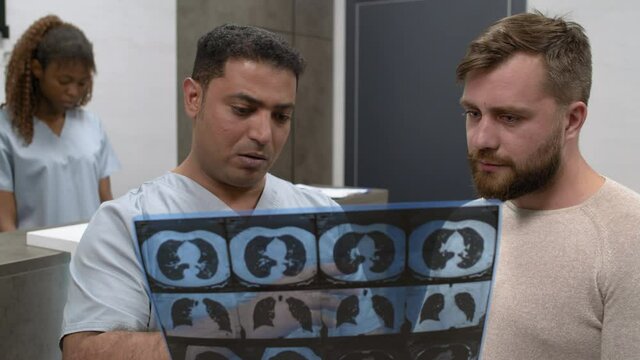 Medium shot of Arab male doctor holding chest CT scan and talking to patient about recovery process