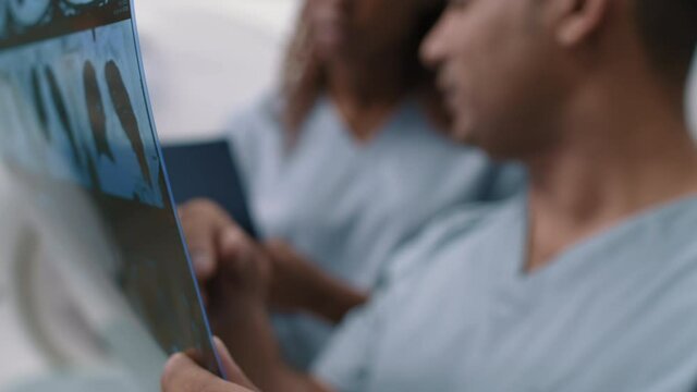 Tilt up with close up of Arab male radiologist reading CT scan of lungs of patient and talking to unrecognizable female tech