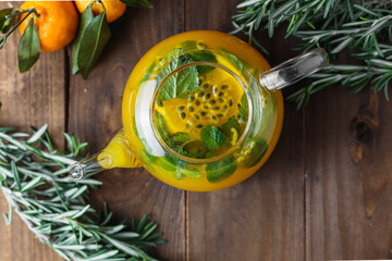 Hot tea with passionfruit and mint in a glass teapot, rosemary and miniature tangerines on the...