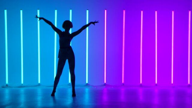 Silhouette of a graceful young woman in full growth dancing elements of modern dance in the studio on a blue purple background with neon lighting. Street dance. Dance poster design. Slow motion.