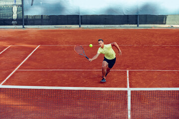 Young handsome man playing tennis on the tennis court