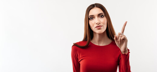 Obraz premium Portrait of Serious girl in casual red sweater showing index finger. Studio shot, white background. Copy space