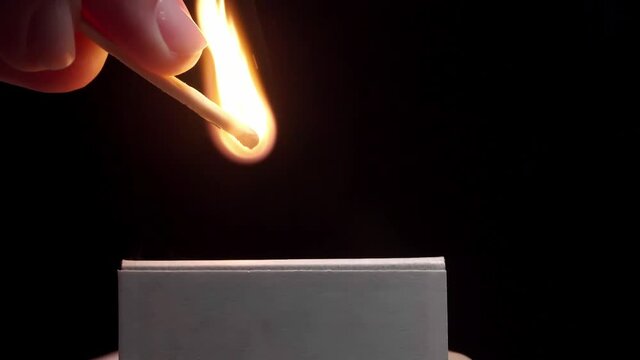 Woman lighting match on dark background, closeup