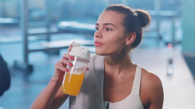 Healthy looking atractive woman bodybuilder drinking juice from sports cup enjoying protein shake intense workout staying in the gym.