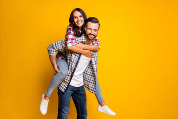 Photo portrait of woman piggyback riding husband isolated on vivid yellow colored background
