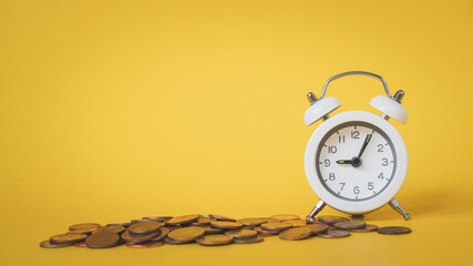 white analog clock with blurred pile of coins on grunge yellow background for business and finance concept , time for savings money concept, banking and business idea