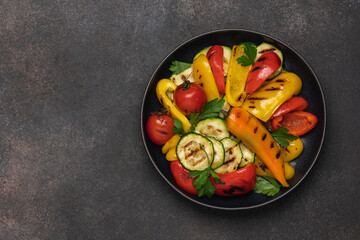Variety of grilled vegetables in bowl on dark background. Zucchini, bell peppers, hot peppers, tomatoes and green parsley