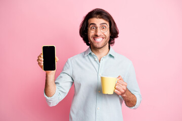 Photo of optimistic funny brown hair guy hold cup show telephone wear spectacles blue shirt isolated on pastel pink color background