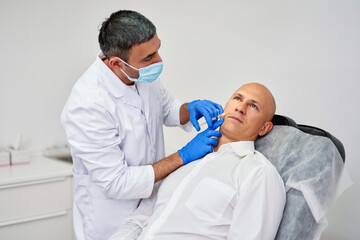 Obraz na płótnie Canvas Cosmetologist making botox injection. Holding syringe. Man is receiving procedure with enjoyment